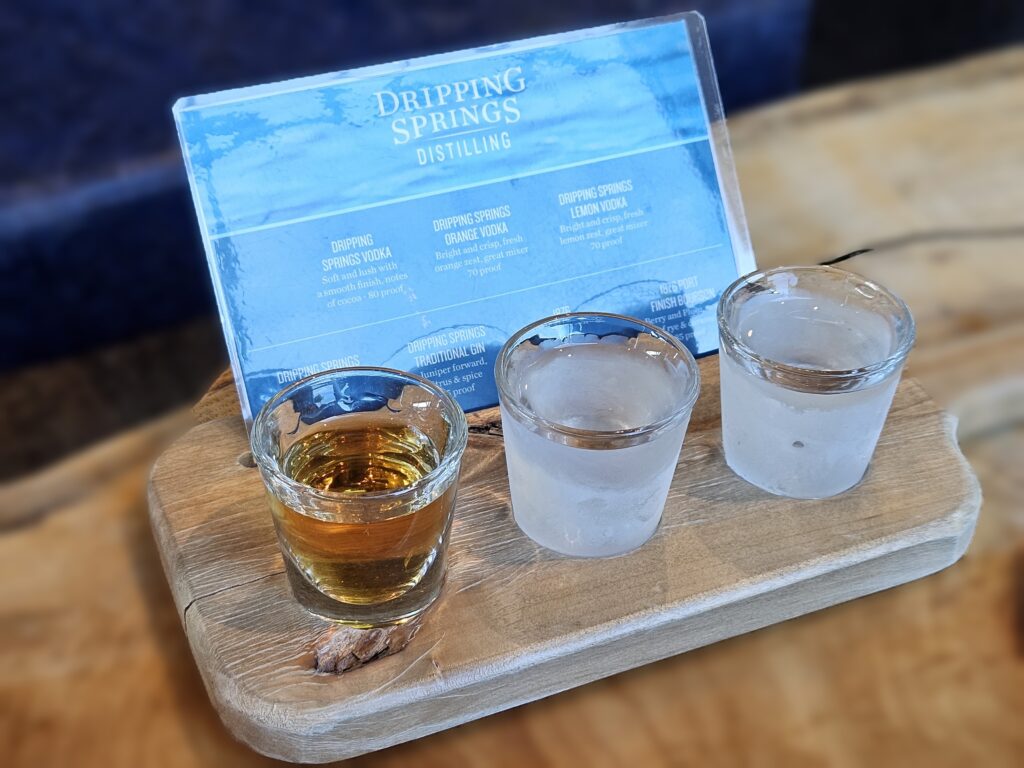 Texas Spirits: image of 3 shot glasses in a wooden paddle with a small blue menu of spirits.